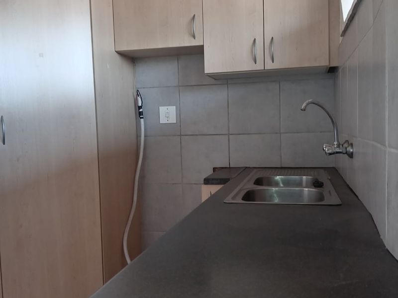 A functional kitchen area featuring light wood-tone cabinetry, dark laminate countertops, a stainless steel sink, and neutral tiled backsplash.