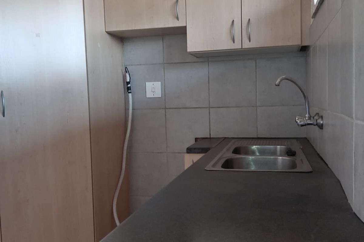 A functional kitchen area featuring light wood-tone cabinetry, dark laminate countertops, a stainless steel sink, and neutral tiled backsplash.