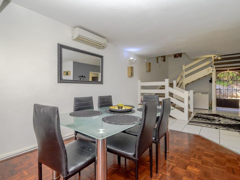 Open-plan dining area featuring parquet flooring, a split-system air conditioner, and a staircase leading to the upper level with a secure entrance.