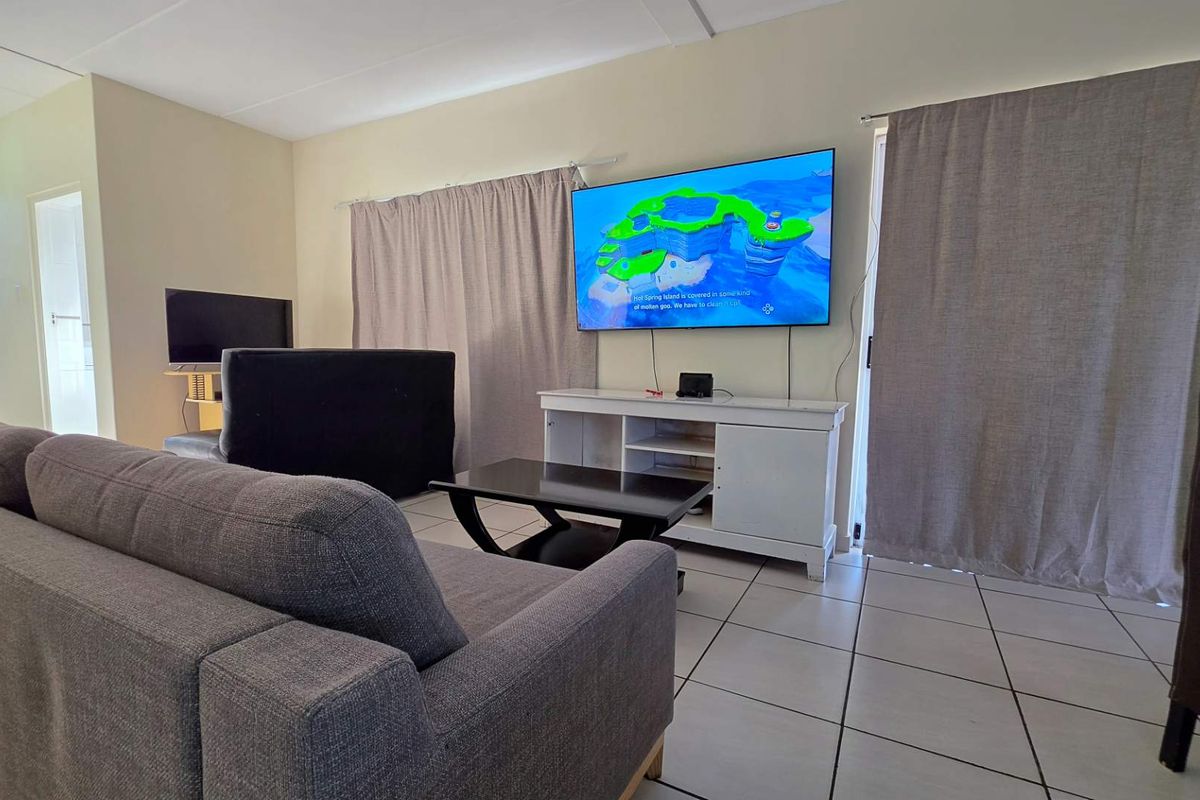 A living room featuring tiled flooring and sliding glass doors with curtains, providing access to an outdoor area.