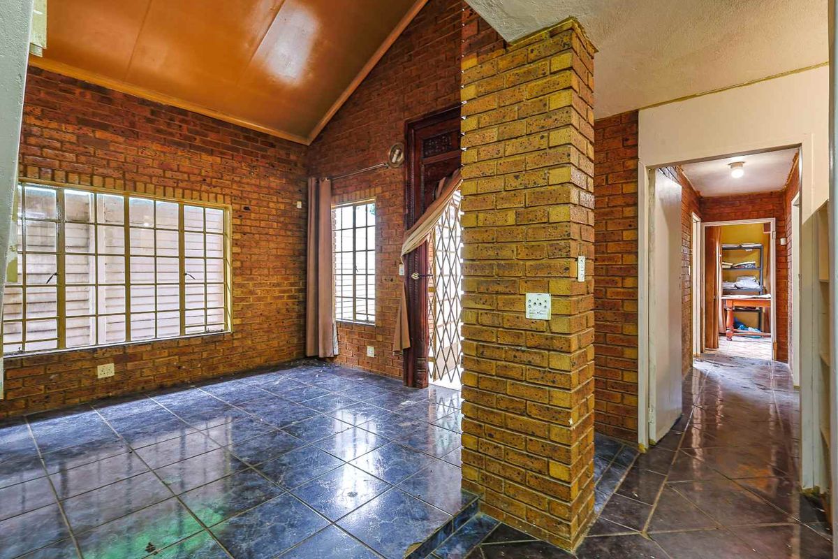 A living area featuring exposed brick walls, vaulted ceilings, and dark tiled flooring, leading into a hallway with access to additional rooms.