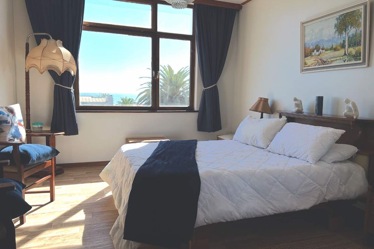 A bright bedroom featuring wood-look flooring, a large window with ocean views, and a built-in wooden headboard.