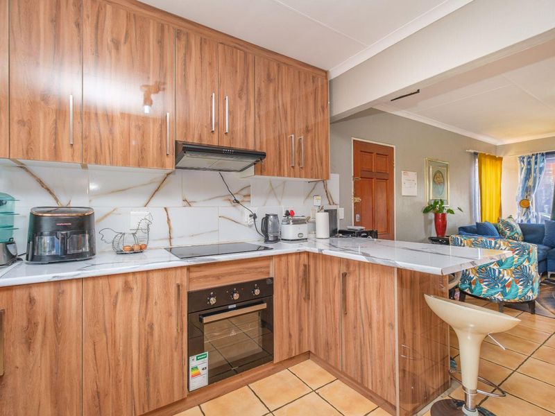 Open-plan kitchen featuring wood-grain cabinetry, marble-effect countertops, and integrated appliances, flowing into the adjacent living area with tiled flooring throughout.
