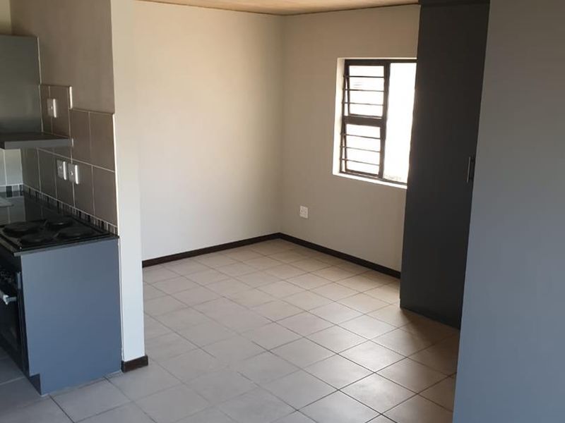 Open-plan living area featuring tiled floors, a compact kitchen with built-in appliances, and a built-in cupboard, offering a functional and versatile space.