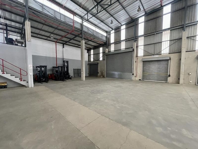 Spacious industrial warehouse featuring high ceilings, multiple roller shutter doors, concrete flooring, and a mezzanine level, suitable for storage or manufacturing operations.