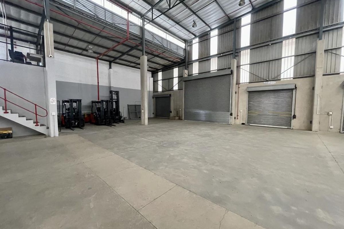 Spacious industrial warehouse featuring high ceilings, multiple roller shutter doors, concrete flooring, and a mezzanine level, suitable for storage or manufacturing operations.