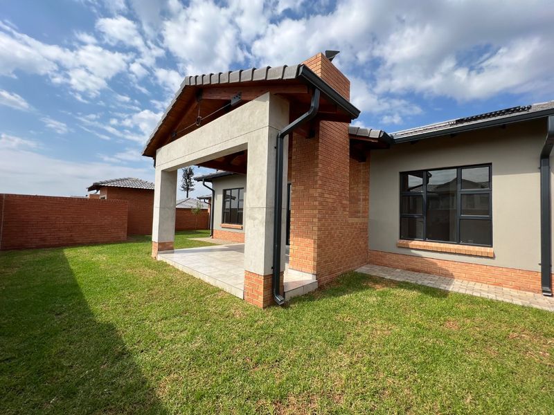 A well-maintained rear exterior view of the townhouse featuring a covered patio, brick chimney, and a neat garden with brick boundary walls.