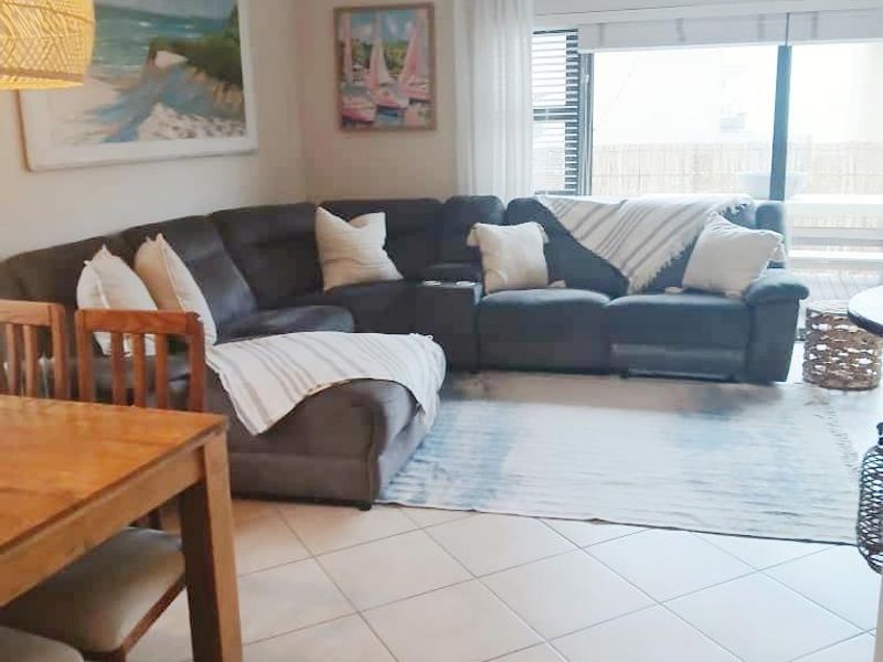 An open-plan living and dining area featuring neutral tiled flooring, large sliding glass doors providing natural light, and classic ceiling cornicing.