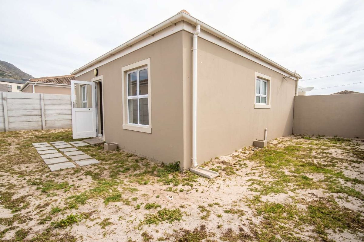 Rear view of the property featuring a small paved area, exterior walls with downpipes, and a surrounding boundary wall with sandy garden space.