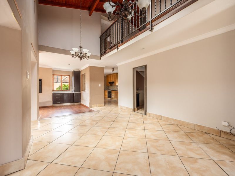 Spacious open-plan living area featuring high ceilings with exposed timber beams, a mezzanine level with wrought iron railing, and tiled flooring throughout.