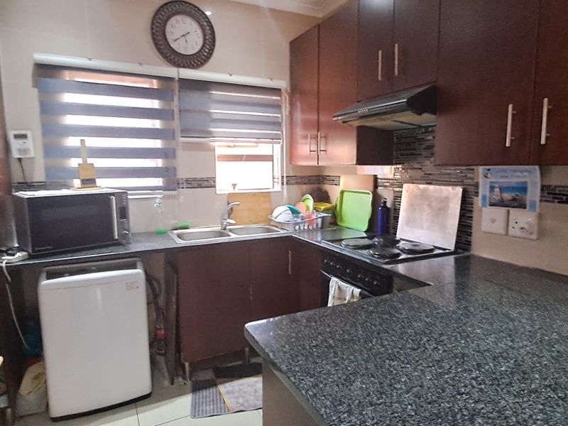 A functional kitchen featuring dark wood cabinetry, granite countertops, a double basin sink, and an integrated electric hob with an extractor fan.