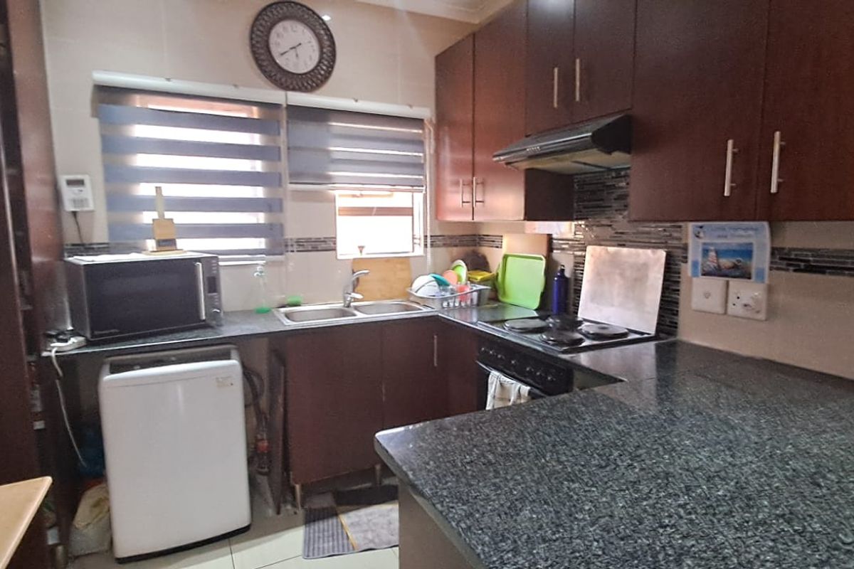 A functional kitchen featuring dark wood cabinetry, granite countertops, a double basin sink, and an integrated electric hob with an extractor fan.
