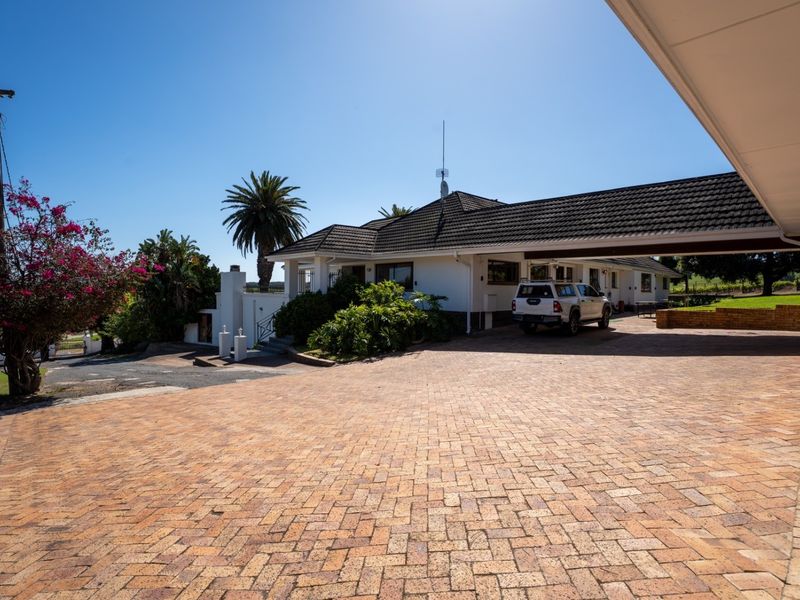 Front view of the farm property featuring a spacious brick-paved driveway and a covered carport area leading to the main residence.
