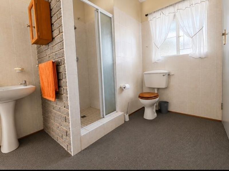 A dated bathroom featuring a pedestal basin, shower enclosure, and toilet, highlighted by an exposed brick feature wall and neutral wall tiling.