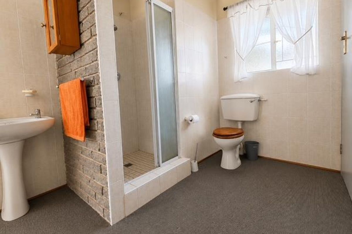 A dated bathroom featuring a pedestal basin, shower enclosure, and toilet, highlighted by an exposed brick feature wall and neutral wall tiling.