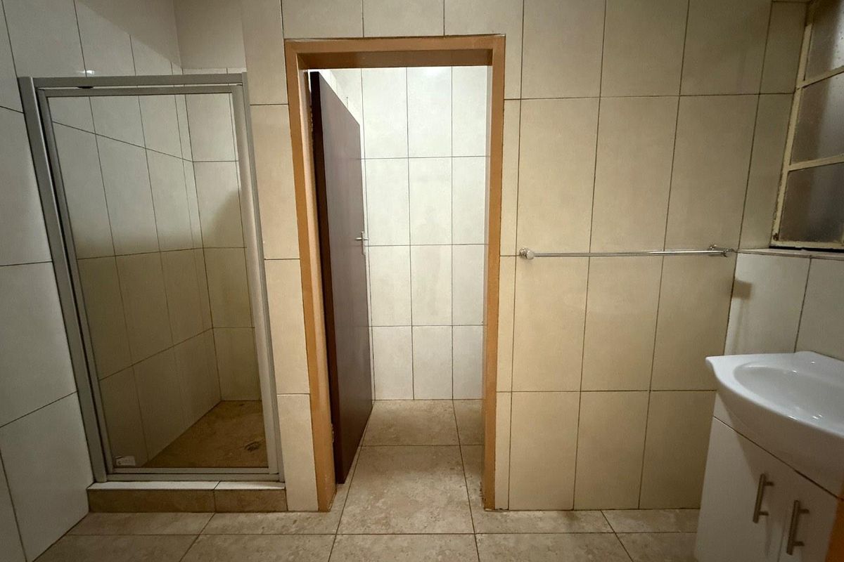A functional bathroom featuring a glass-enclosed shower, tiled walls and flooring, a vanity basin, and a separate doorway leading to an adjacent space.