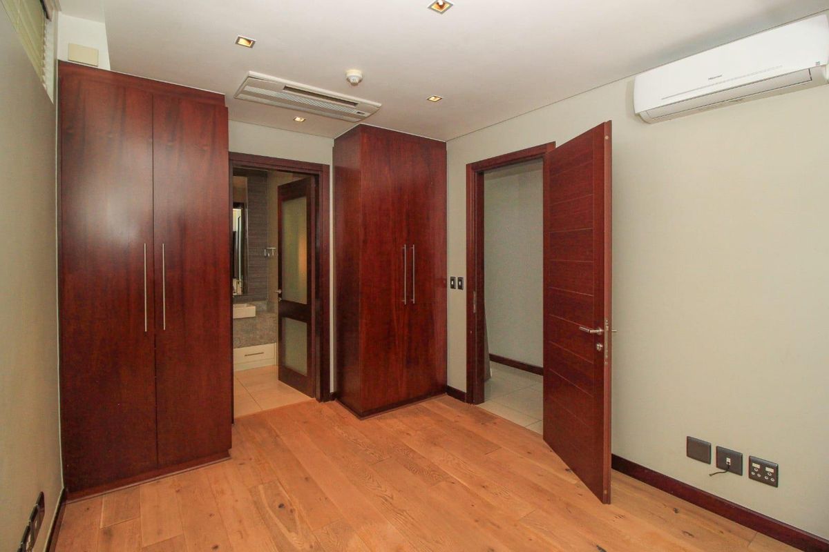 A bedroom featuring warm-toned wooden flooring, built-in dark wood cabinetry, recessed ceiling lighting, and a wall-mounted air conditioning unit.