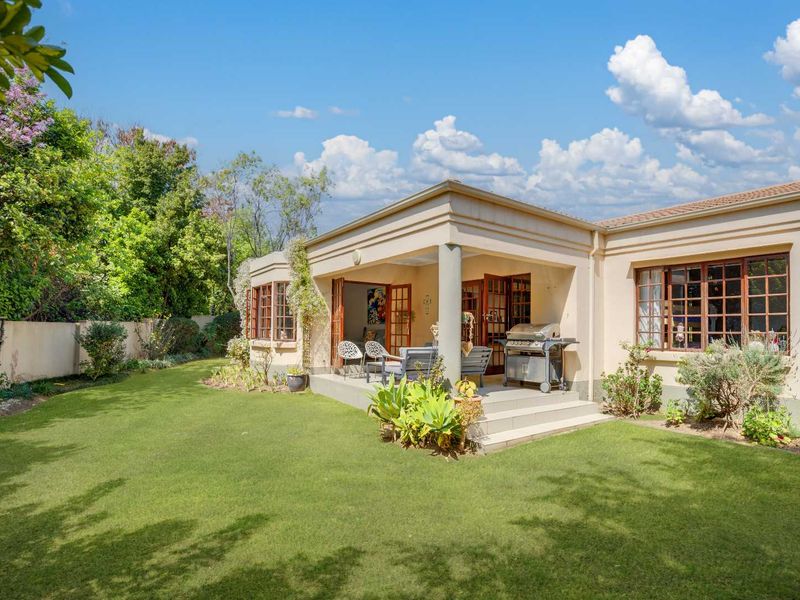 A well-maintained rear exterior view featuring a covered patio, landscaped garden, and classic multi-pane windows, offering a seamless transition between indoor and outdoor living spaces.