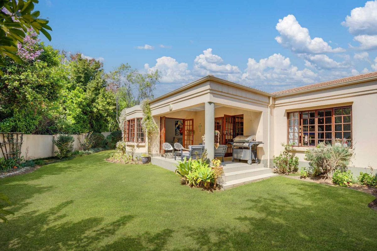 A well-maintained rear exterior view featuring a covered patio, landscaped garden, and classic multi-pane windows, offering a seamless transition between indoor and outdoor living spaces.