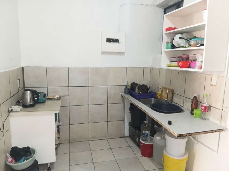 A functional kitchen area featuring tiled splashbacks, a stainless steel sink, and open shelving, requiring cosmetic updates to improve its overall condition and aesthetic appeal.