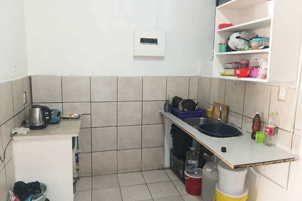 A functional kitchen area featuring tiled splashbacks, a stainless steel sink, and open shelving, requiring cosmetic updates to improve its overall condition and aesthetic appeal.
