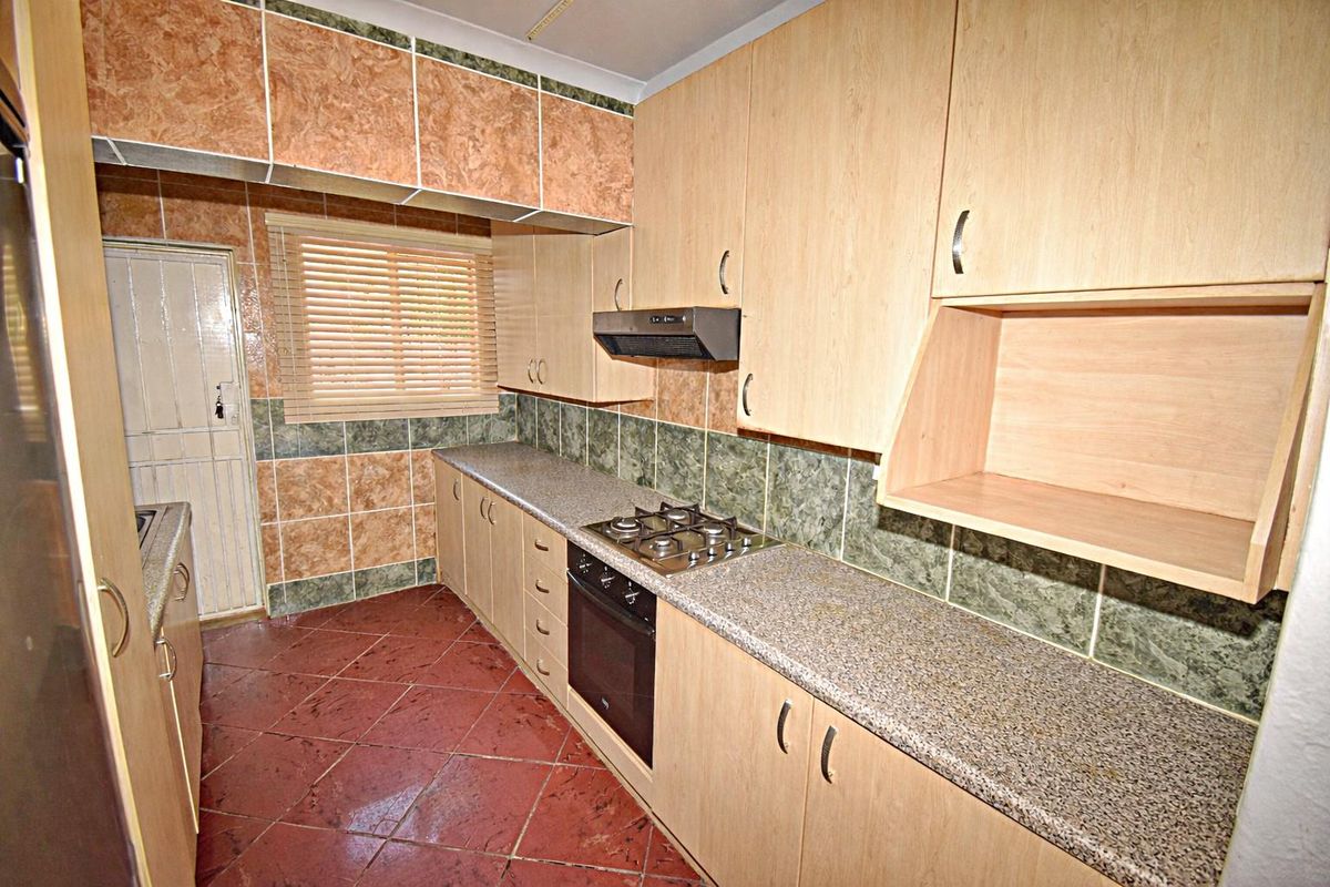 A functional kitchen featuring light wood cabinetry, granite-look countertops, a built-in oven with gas hob, and tiled flooring.