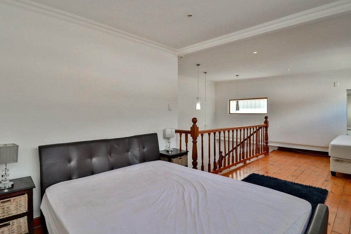 Spacious bedroom featuring polished timber flooring, a wooden balustrade overlooking the lower level, and recessed ceiling lighting.