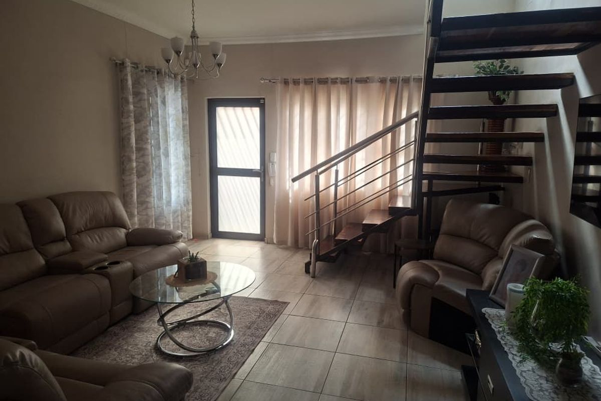 A living room featuring tiled flooring, a staircase with wooden treads and metal railings, and a glass-paneled exterior door.