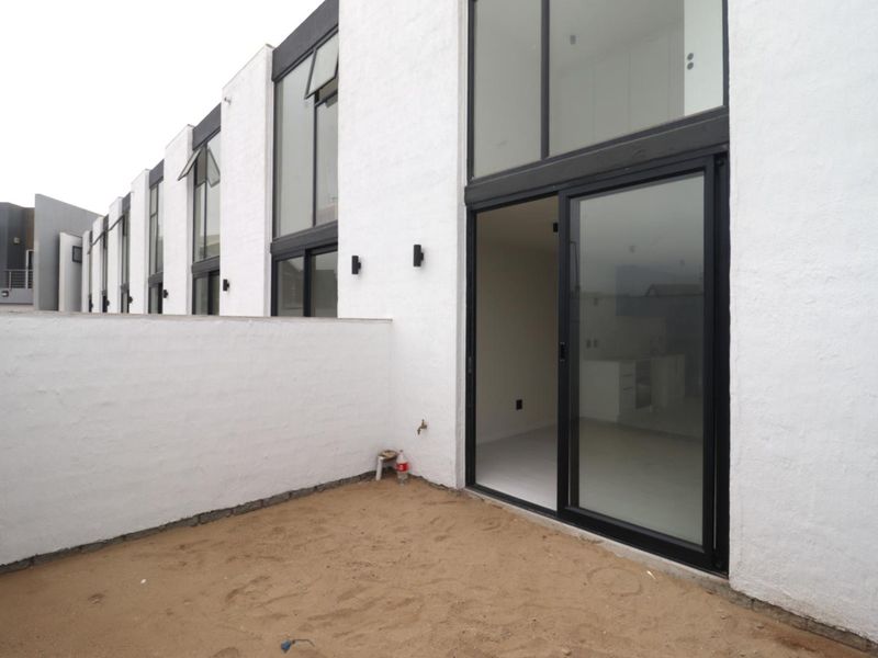 Rear view of a modern apartment complex featuring white textured facades, large glass sliding doors, and an unfinished ground area.