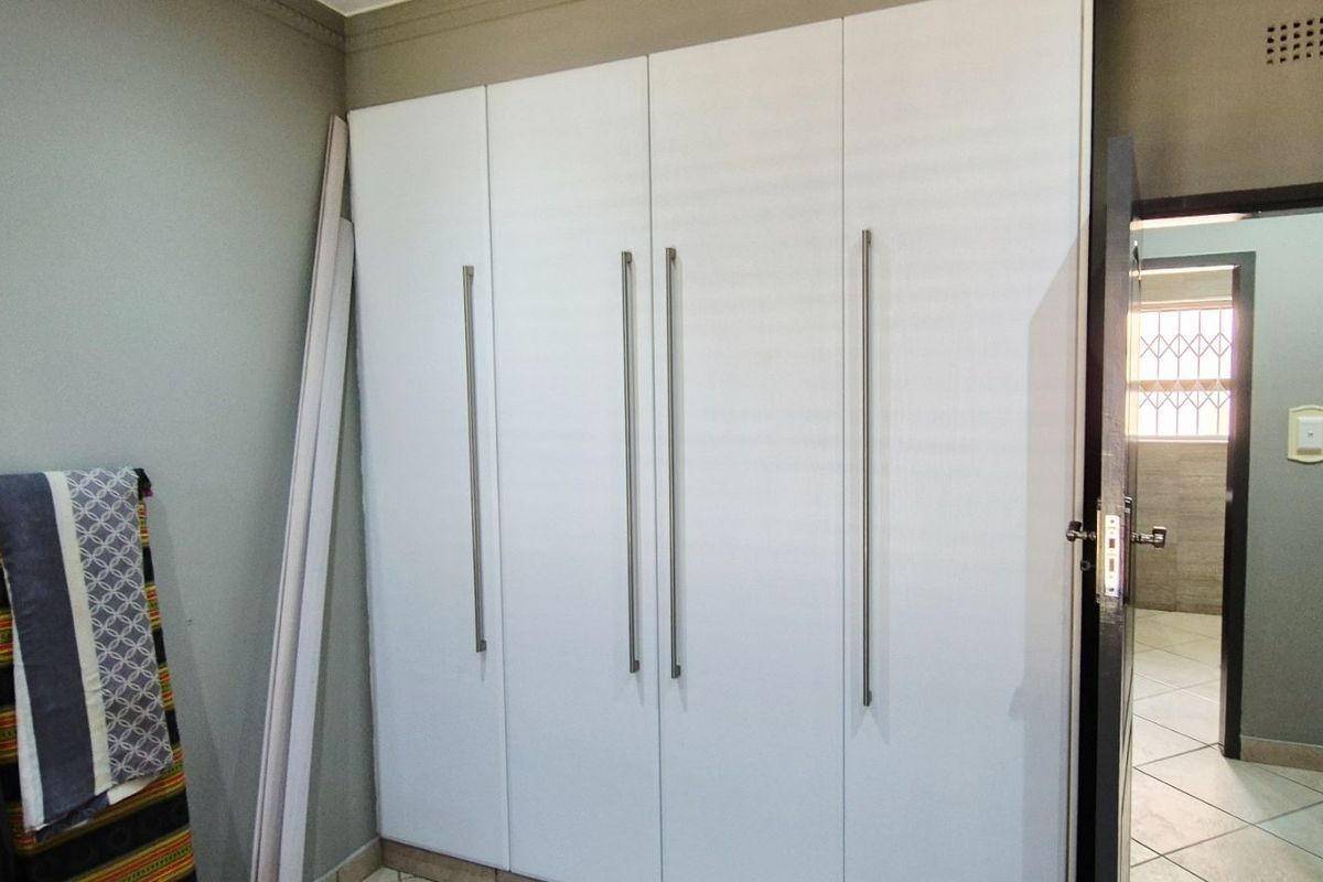 A bedroom featuring modern white built-in cupboards with long vertical handles and neutral wall tones.