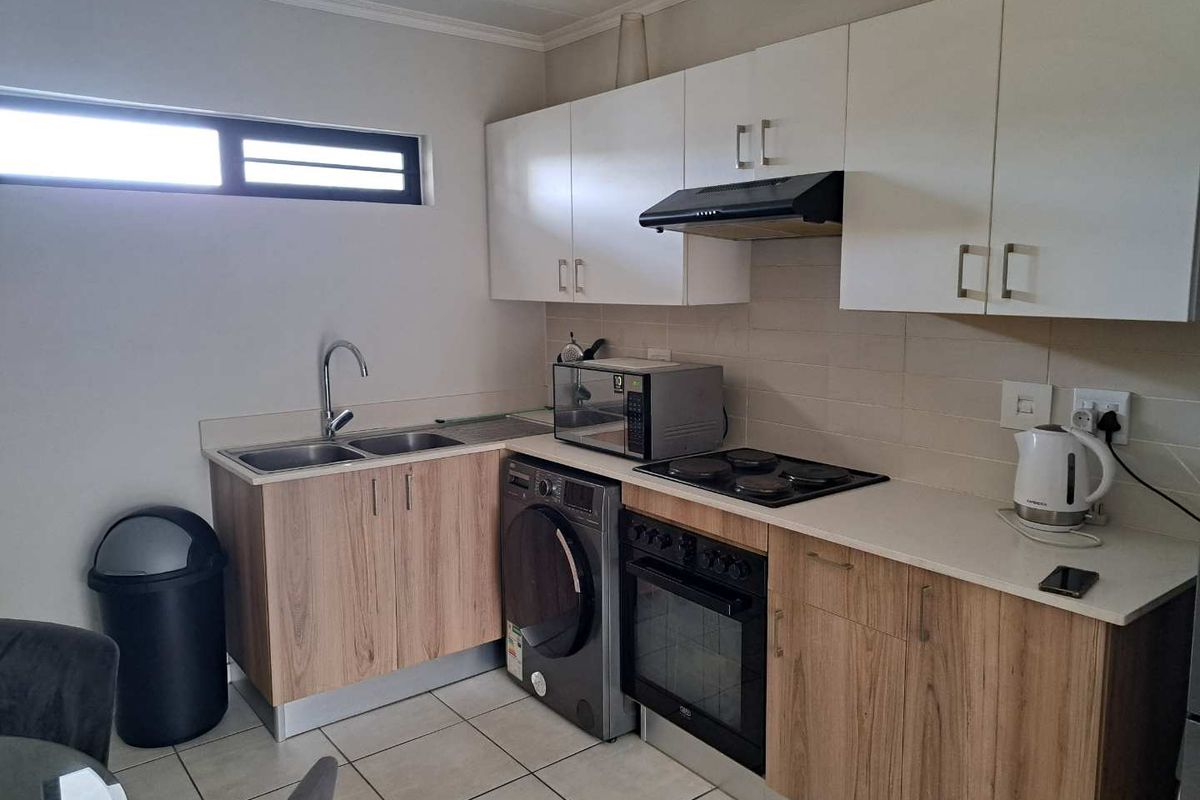 Compact kitchen featuring light wood-finish cabinetry, white upper cabinets, tiled backsplash, built-in oven, hob, extractor fan, and a double sink.
