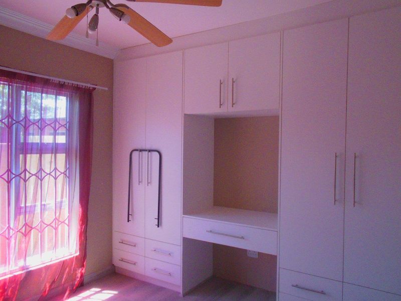 A bedroom featuring extensive built-in cabinetry with an integrated desk area, ceiling fan, and natural light from the window.