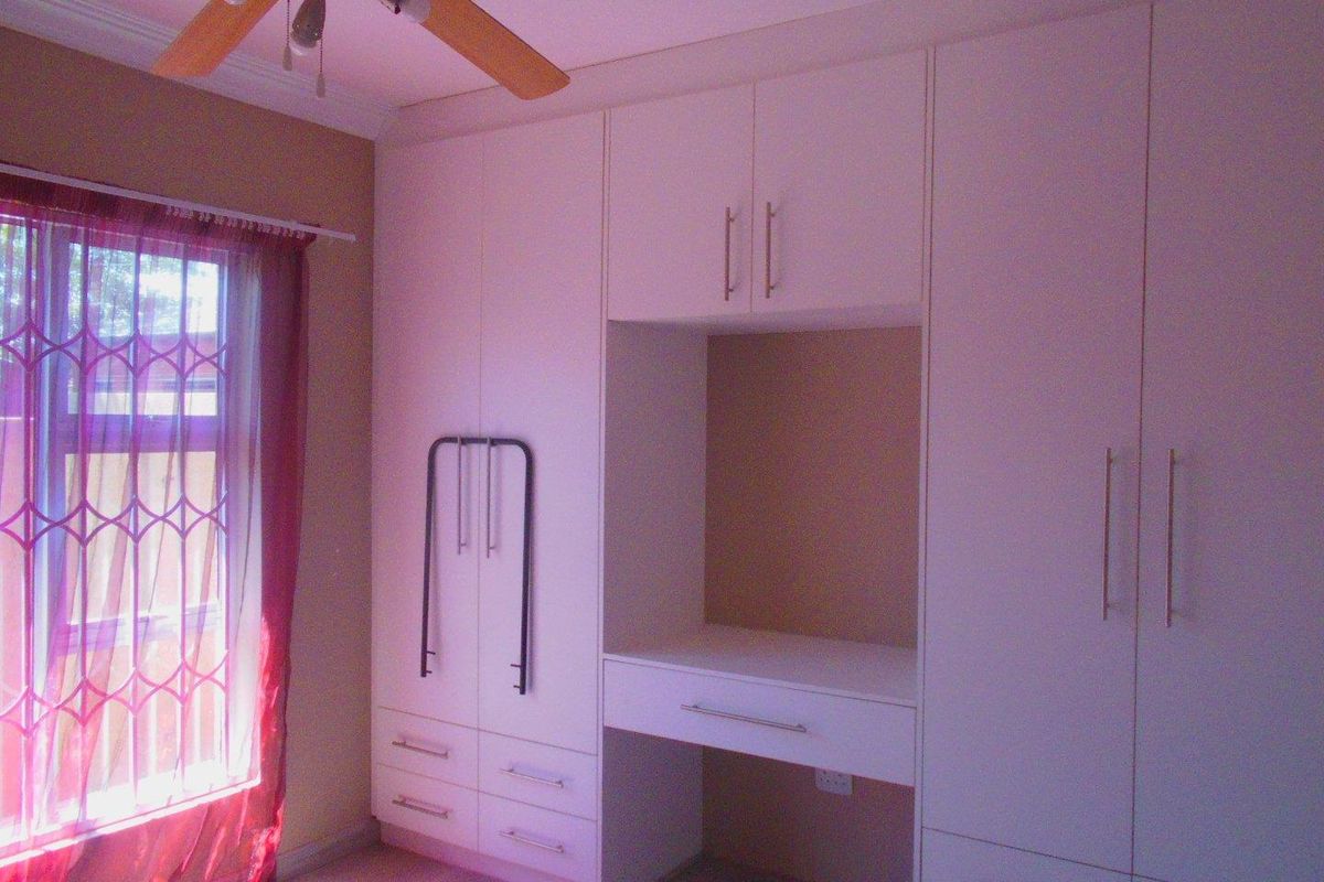 A bedroom featuring extensive built-in cabinetry with an integrated desk area, ceiling fan, and natural light from the window.