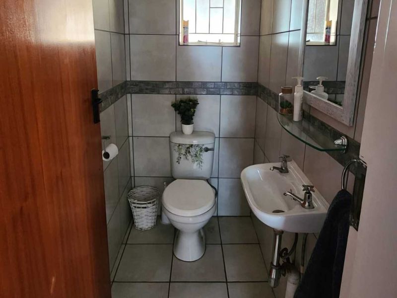 A compact bathroom featuring tiled walls and floors, a pedestal washbasin, and a standard toilet with a window for natural light.