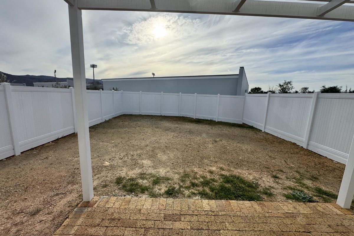 A rear outdoor space featuring a brick paved patio, a white pergola, and a fully enclosed white vinyl privacy fence with an unlandscaped yard.