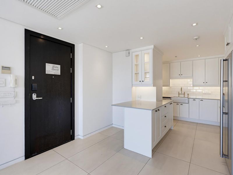 A modern, well-maintained kitchen featuring white cabinetry, a central island, subway tile backsplash, and an apron sink, adjacent to the main entrance.