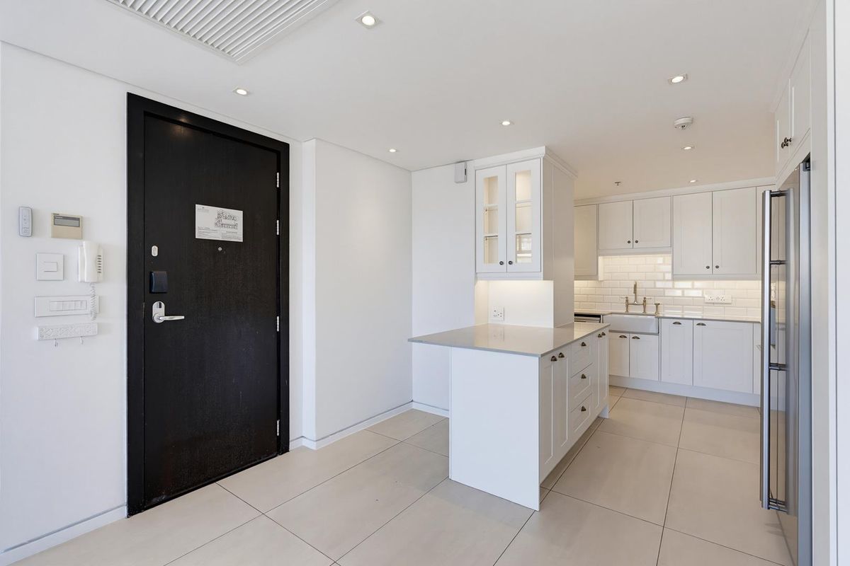 A modern, well-maintained kitchen featuring white cabinetry, a central island, subway tile backsplash, and an apron sink, adjacent to the main entrance.