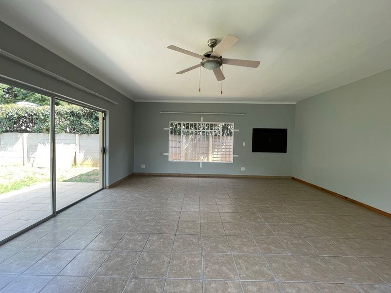 Spacious, empty living area featuring neutral tiled flooring, a ceiling fan, and large sliding glass doors providing access to the rear garden.