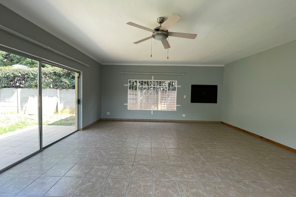 Spacious, empty living area featuring neutral tiled flooring, a ceiling fan, and large sliding glass doors providing access to the rear garden.
