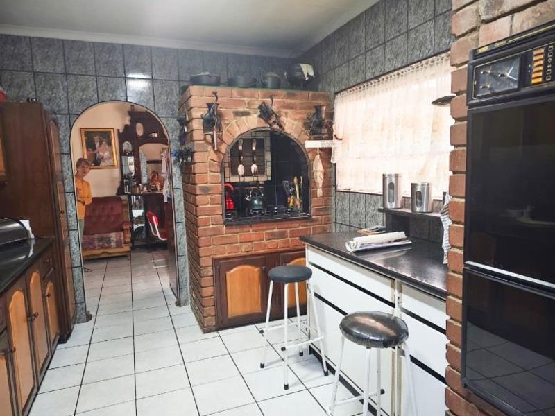 A dated kitchen featuring a unique built-in brick oven enclosure, tiled walls, and integrated wall oven, offering significant potential for a modern renovation.