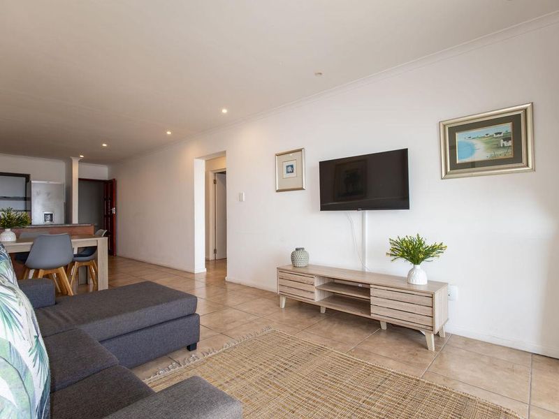 Open-plan living area featuring neutral walls, recessed downlighting, and ceramic floor tiles, providing a functional and connected space for relaxation and dining.