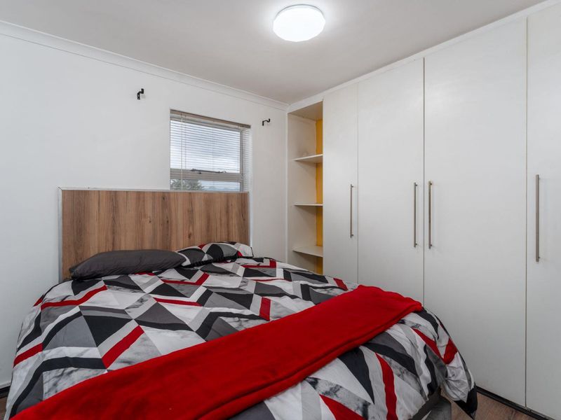 A well-maintained bedroom featuring ample built-in wardrobe storage with integrated open shelving and a window fitted with venetian blinds.
