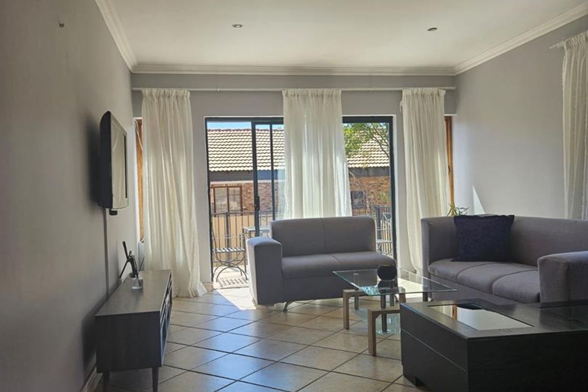 A well-lit living room featuring tiled flooring, recessed downlighting, and sliding glass doors that provide access to an outdoor patio area.