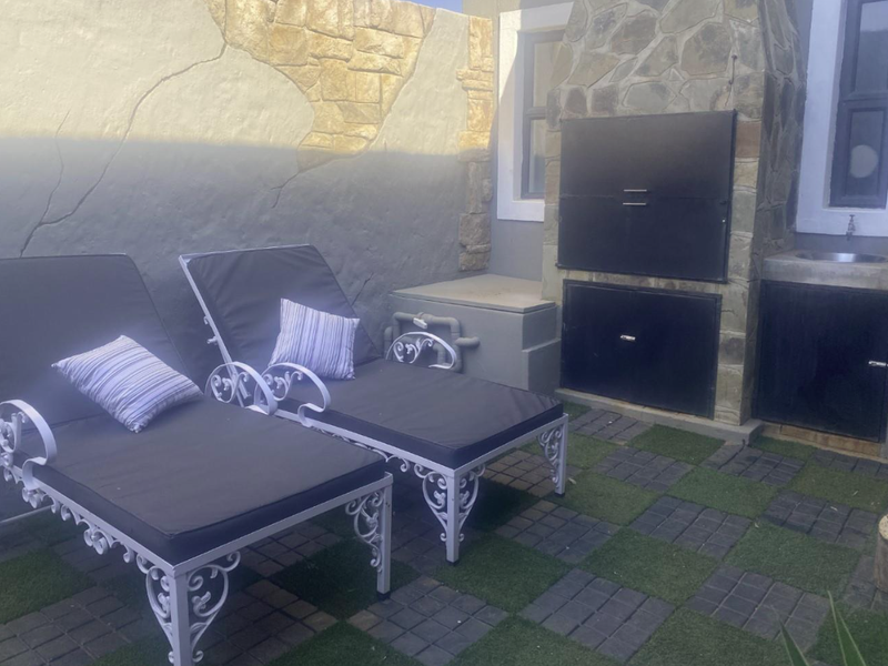 Outdoor patio area featuring a built-in braai, stone cladding, and a small integrated sink, set on a paved and artificial grass surface.