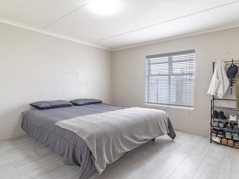 A simple bedroom featuring light-toned laminate flooring and a window fitted with venetian blinds.