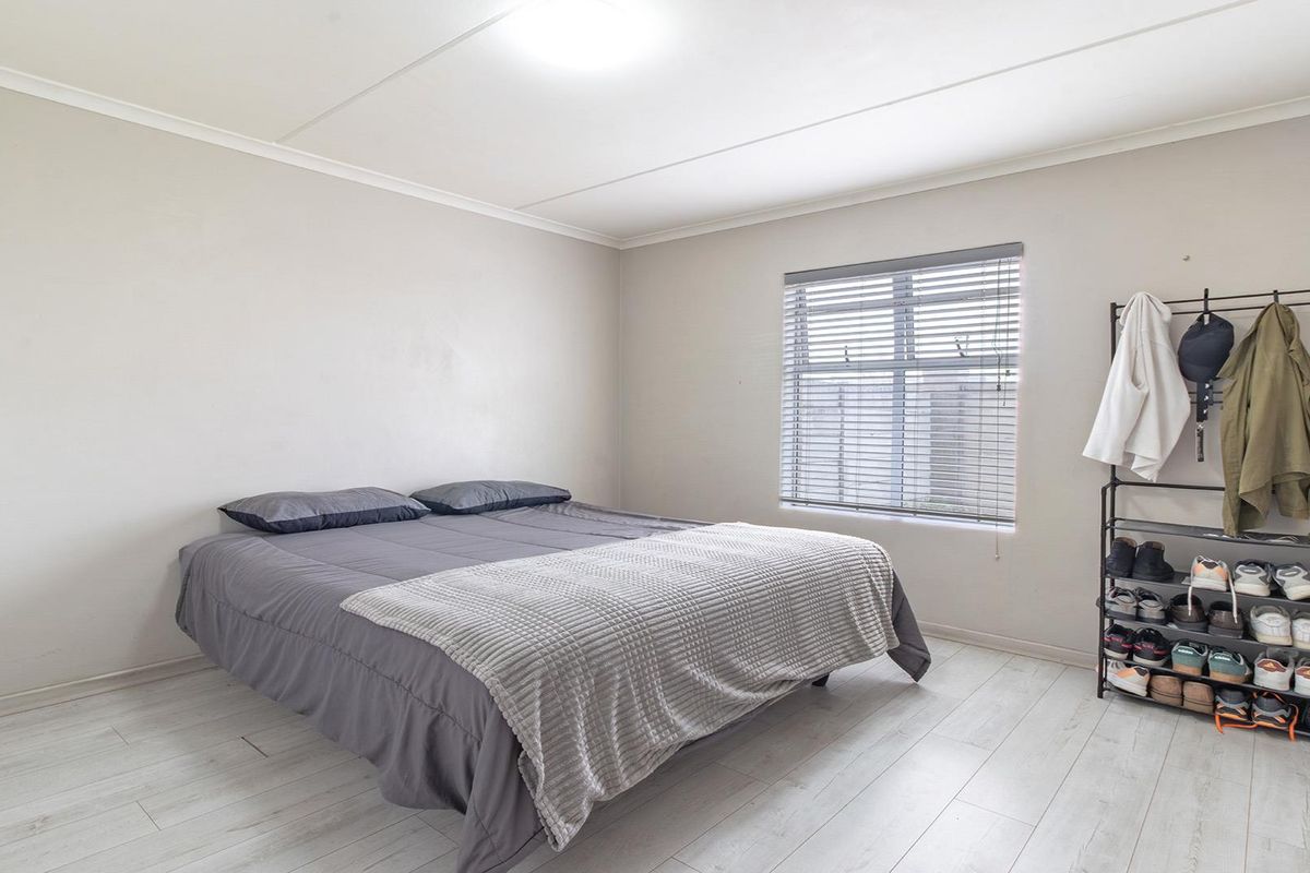 A simple bedroom featuring light-toned laminate flooring and a window fitted with venetian blinds.