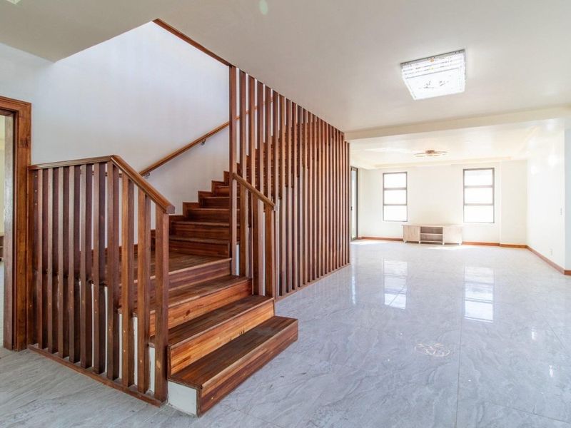 Spacious open-plan living area featuring a striking timber staircase with slatted balustrade and polished tiled flooring throughout.