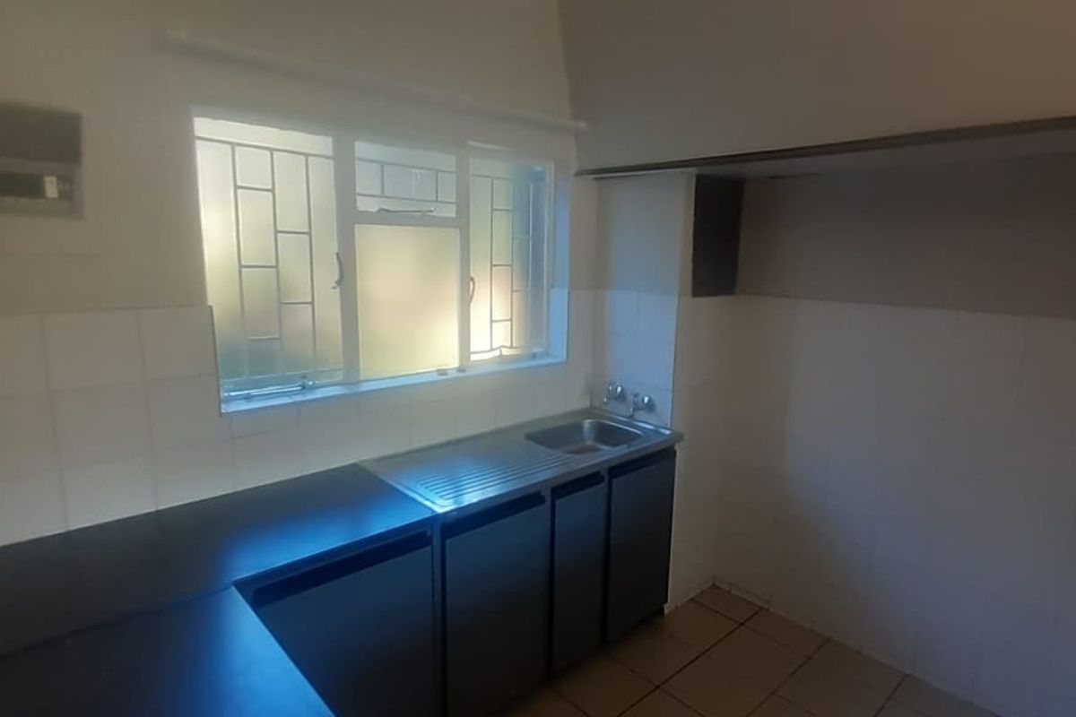 A functional kitchen area featuring dark cabinetry, a stainless steel sink, tiled splashbacks, and a window with security bars.