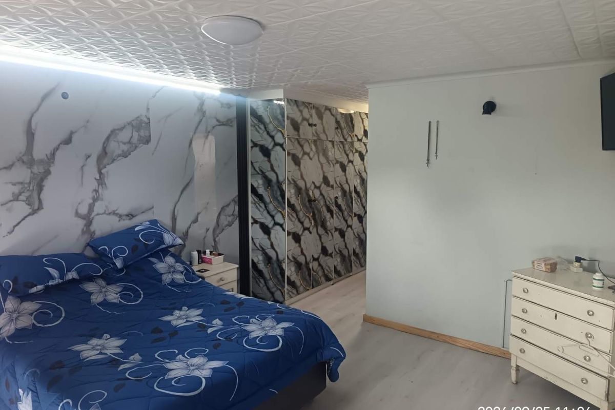 Bedroom featuring built-in marble-effect cupboards, laminate flooring, and textured ceiling tiles. The space offers functional storage and neutral finishes.