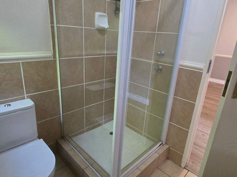 A functional bathroom featuring a tiled shower enclosure and a standard toilet, finished with neutral wall and floor tiles.